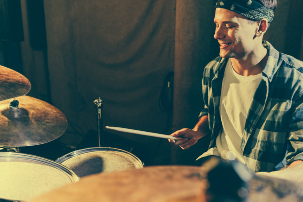selective focus of cheerful drummer holding drum sticks while playing drums  - Foto, Imagem