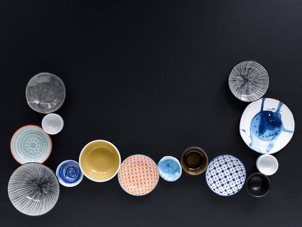 collection of white and colored tableware on black background  - Fotografie, Obrázek