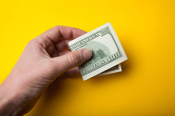 Bent hundred dollar bill in hand on a yellow background, sale or - Φωτογραφία, εικόνα