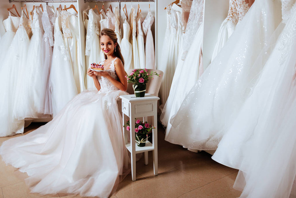 Atraente jovem noiva está sorrindo ao escolher o vestido de noiva
 - Foto, Imagem