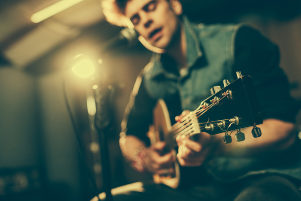 selective focus of acoustic guitar in hands of singer near microphone  - Fotografie, Obrázek