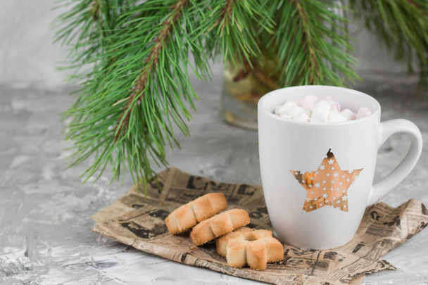 mug with drink decorated with marshmallow and star shape cookies  near evergreen christmas tree branches gray concrete background - Foto, imagen
