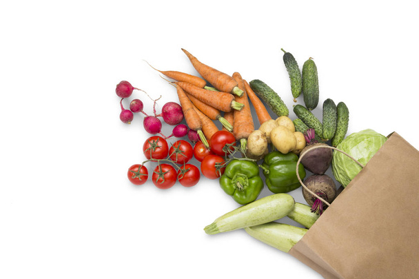 Paperi ostoskassi ja tuoreita luomuvihanneksia valkoisella taustalla. Käsite ostaa maatilan vihanneksia, huolehtia terveydestä, kasvissyönnistä. Maalaistyyliin. Tasainen, ylhäältä
 - Valokuva, kuva