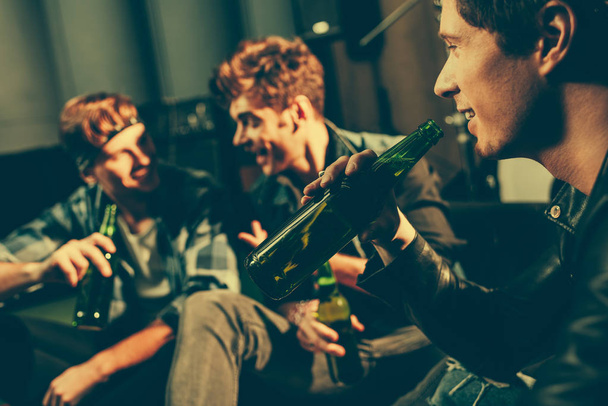 selective focus of man holding bottle with beer and looking at friends  - Foto, imagen