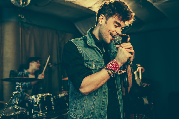 selective focus of trendy singer singing in microphone near rock band  - Photo, Image