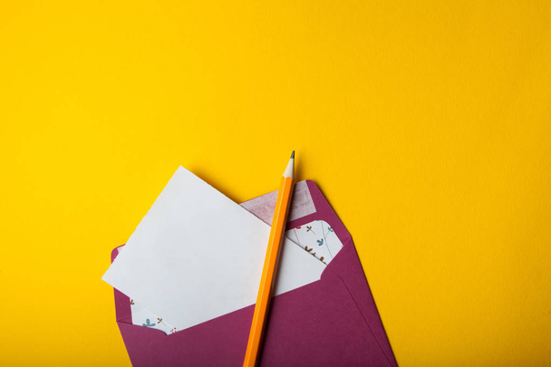 Envelope, white sheet of paper and pencil on a yellow background - Foto, afbeelding