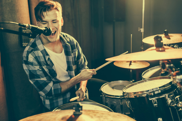 selective focus of handsome drummer singing in microphone while playing drums  - Photo, Image