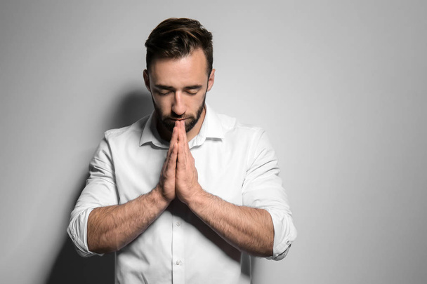 Religious young man praying to God on light background - Foto, Imagen