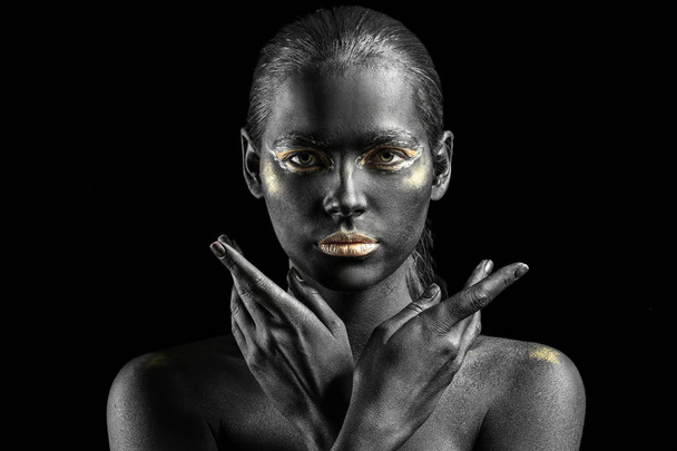 Beautiful woman with black and golden paint on her body against dark background - Foto, Imagem