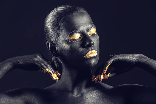 Beautiful woman with black and golden paint on her body against dark background - Фото, изображение