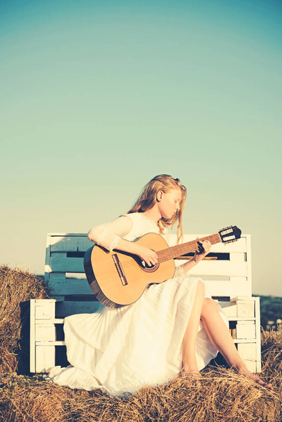 Woman guitarist perform music concert. Fashion musician in white dress on sunny nature. Albino girl hold acoustic guitar, string instrument. Sensual woman play guitar on wooden bench - Zdjęcie, obraz
