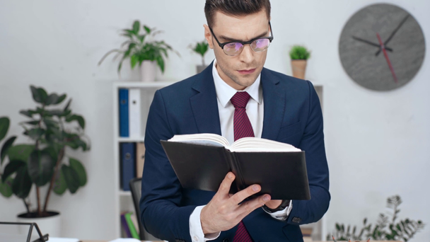 good-looking businessman in eyeglasses reading notebook, smiling and looking at camera  - Footage, Video
