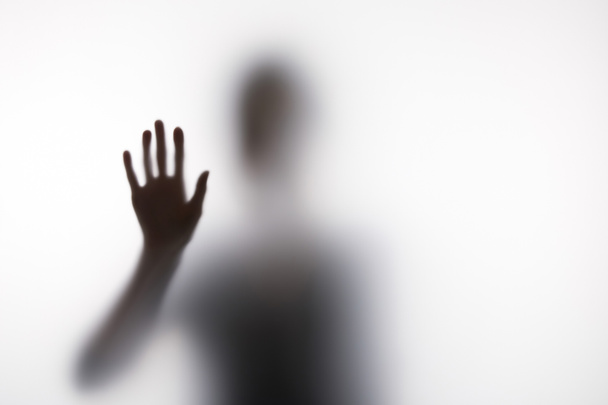 Blurry silhouette of person touching glass with hand - Photo, Image