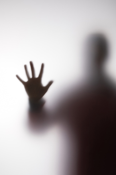 Blurry silhouette of person touching glass with hand - Foto, afbeelding