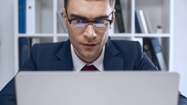 przystojny, uważny biznesmen w okularach za pomocą laptopa w biurze - Materiał filmowy, wideo