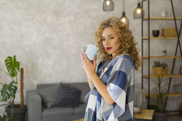Portrait of young blonde woman at bright kitchen drinking cup of tea or coffee - Fotoğraf, Görsel