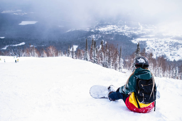 Female snowboarder freerider with snowboard in the mountains sitting on a snowy slope - Foto, Imagen
