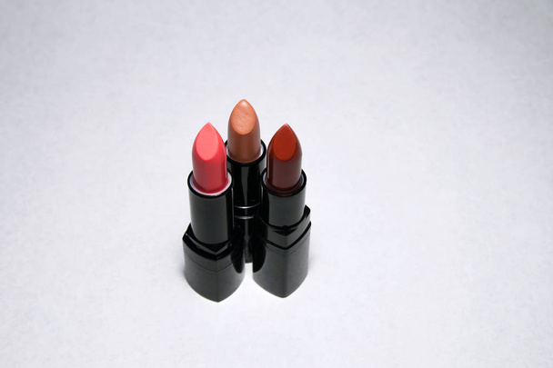 Three pink, beige and carrot lipsticks stand vertically on a white background - Fotó, kép