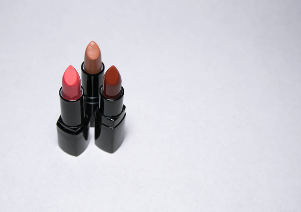 Three lipsticks stand vertically on a white background close to each other in the left side - Φωτογραφία, εικόνα