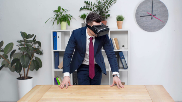 άνθρωπος των επιχειρήσεων στο σετ κεφαλής εικονικής πραγματικότητας που βλέπουν άδειο ξύλινο γραφείο σε γραφείο - Πλάνα, βίντεο