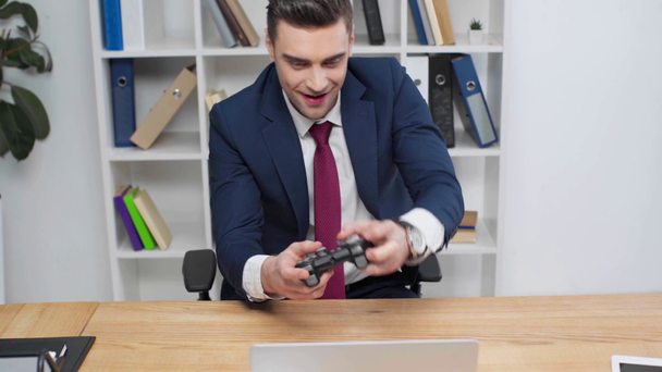 excited businessman playing video game while sitting at workplace in office - Footage, Video