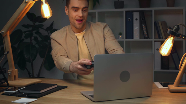 возбужденный бизнесмен играет в видеоигры и показывает да жест во время установки на рабочем месте в темном офисе ночью
 - Кадры, видео