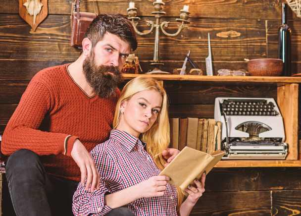 Couple in love reading poetry in warm atmosphere. Lady and man with beard on dreamy faces with book, reading romantic poetry. Romantic evening concept. Couple in wooden vintage interior enjoy poetry - Photo, image