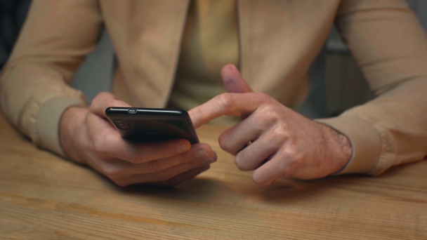 selective focus of businessman using smartphone while sitting at wooden desk - Metraje, vídeo