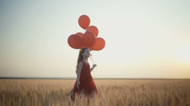 happy young girl with balloons running in the wheat field at sunset. 4k video. - Materiał filmowy, wideo