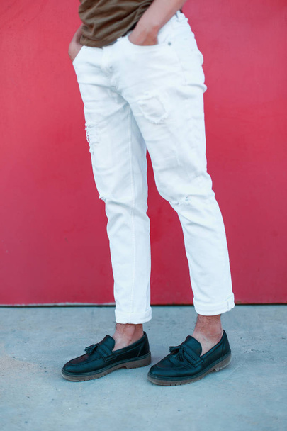 Tyylikäs nuori mies seisoo lähellä metallista vintage kirkas vaaleanpunainen seinä. Nahka mustat kengät ja tyylikäs valkoinen housut. Muodikas kausiluonteinen miesten kengät
. - Valokuva, kuva