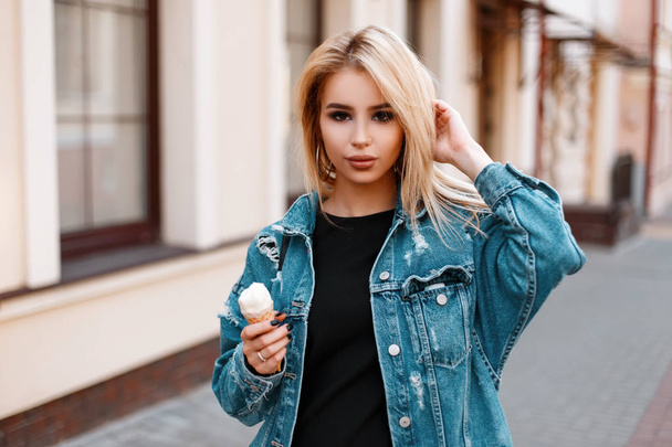 Stylová krásná mladá dáma v módních letních džíních s sladkou zmrzlinou chodí po městě poblíž starobylových budov. Atraktivní roztomilá modelka, užívající si víkend. - Fotografie, Obrázek