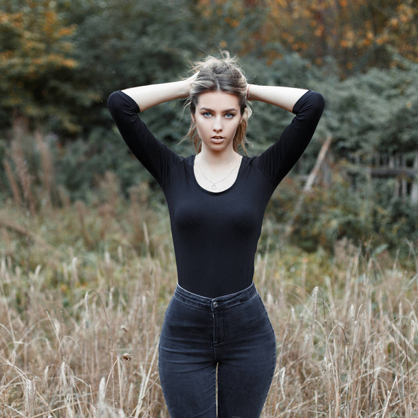 Atrakcyjne całkiem piękna młoda kobieta w stylowej koszulce w vintage jeans stojący w polu wśród suchej trawy. Sexy dziewczyna na zewnątrz odpoczynek na wsi. Ciepły, jesienny dzień. - Zdjęcie, obraz