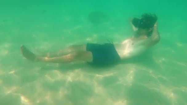 Podwodne strzał młodego człowieka używać zestawu słuchawkowego Vr, Układanie na dno morza. Osoba nosząca okulary vr czuje się ina tropikalne morze. Pojęcie rzeczywistości rozszerzonej - Materiał filmowy, wideo