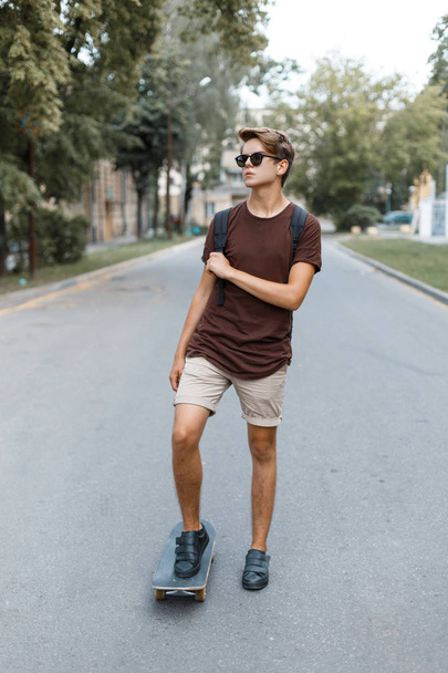 Young stylish handsome hipster man in fashionable summer clothes is riding on a snowboard. American cool modern guy actively spends the weekend. - Photo, Image