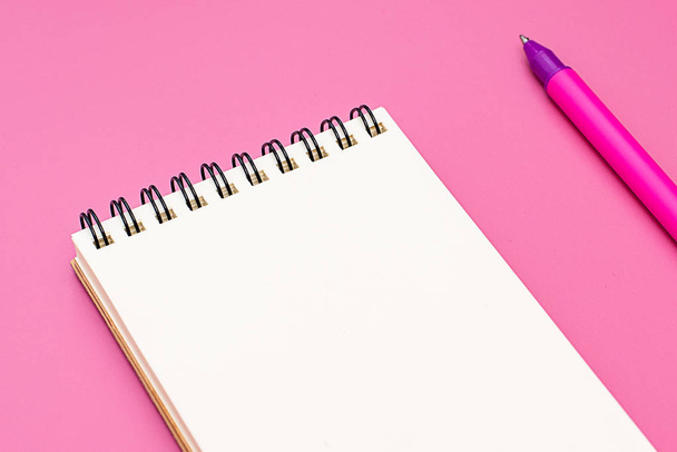 Cuaderno en blanco con espiral para la aplicación de etiquetas y bolígrafo sobre fondo rosa
 - Foto, Imagen