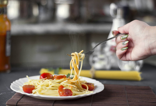 Steamed pasta spaghetti on a fork in tomato sauce with cheese and parsley, female hand. Italian spaghetti pasta on a dark stone background. - Foto, afbeelding