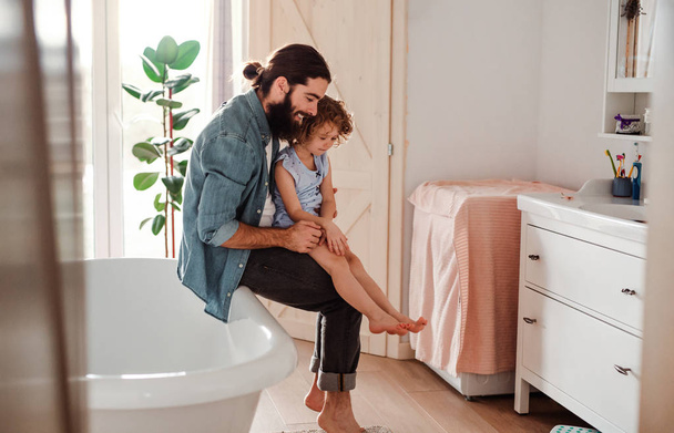 A small girl with young father in bathroom at home, looking at painted nails. - Foto, afbeelding