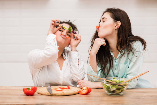 Due ragazze fanno facce divertenti con verdure in cucina
 - Foto, immagini