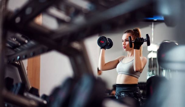 Young girl or woman with dumbbells, doing workout in a gym. - Foto, Imagem