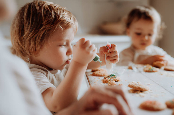 Two small toddler children sitting at the table, decorating and eating cakes at home. - Foto, afbeelding