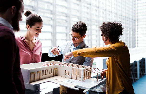 Group of young architects with model of a house standing in office, talking. - 写真・画像