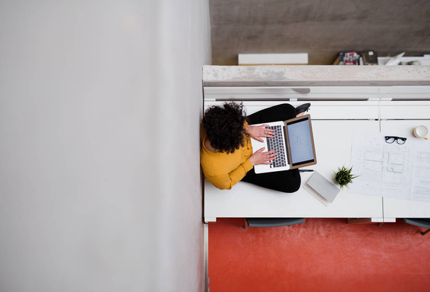 Una vista dall'alto di una giovane donna d'affari seduta sulla scrivania in un ufficio, utilizzando il computer portatile
. - Foto, immagini