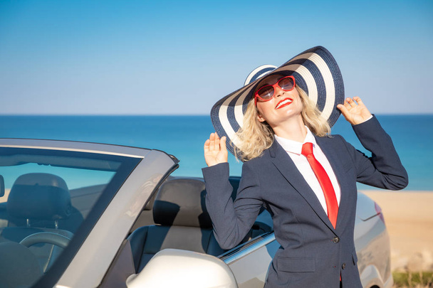 Successful young businesswoman on beach. Woman standing near cabriolet classic car. Summer vacations and freedom travel concept - 写真・画像
