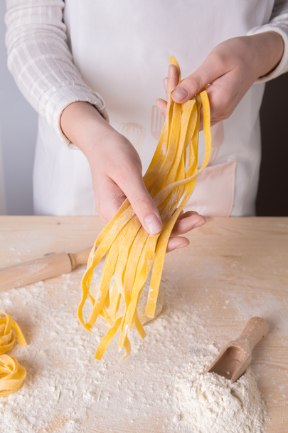 Tagliatelle de pasta casera cruda italiana fresca en manos de una mujer joven. Concepto de pasta italiana
 - Foto, Imagen