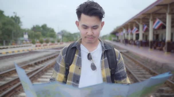 Проводя отпуск и ожидая поезда на железнодорожной станции, молодой мужчина-турист с рюкзаком наслаждается путешествием. Концепция путешествий мужчин
. - Кадры, видео