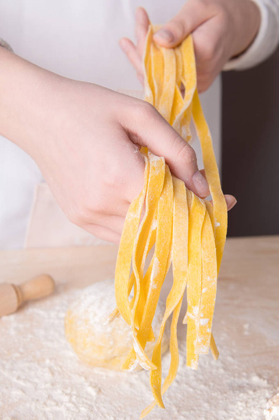 Свежая итальянская сырая домашняя паста тальятелле в руках молодой женщины. Итальянская паста
 - Фото, изображение