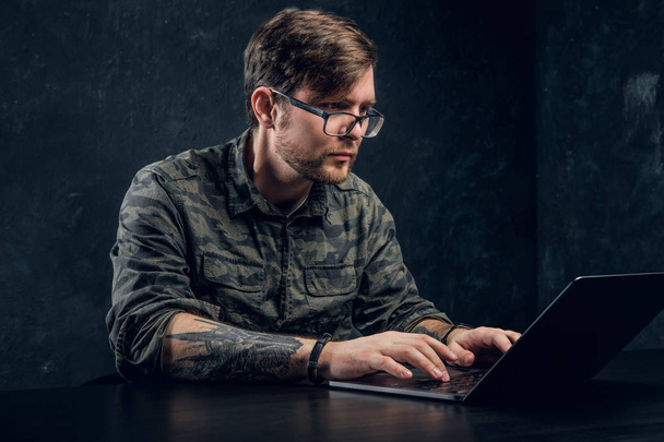 Bebaarde hacker in glazen maakt hacken vergadering achter een laptop - Foto, afbeelding