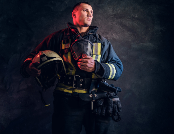 Brutal bombero mira hacia los lados y sostiene un casco en su mano
  - Foto, imagen