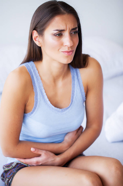 Πόνος στο στομάχι. Ανθυγιεινά νεαρή γυναίκα με στομαχόπονο ακουμπά στο κρεβάτι στο σπίτι - Φωτογραφία, εικόνα