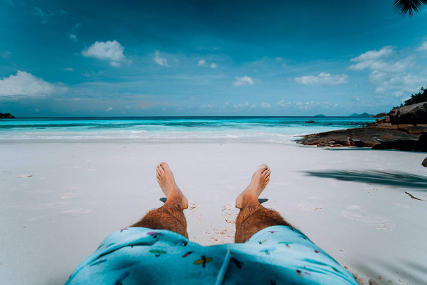 Travel vacation background male legs with swim short on paradise white sand tropical beach in front of turquoise sea. Exotic holidays - Fotografie, Obrázek